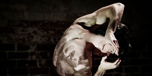 Alex O'Neill in darkness with projections cast on his body