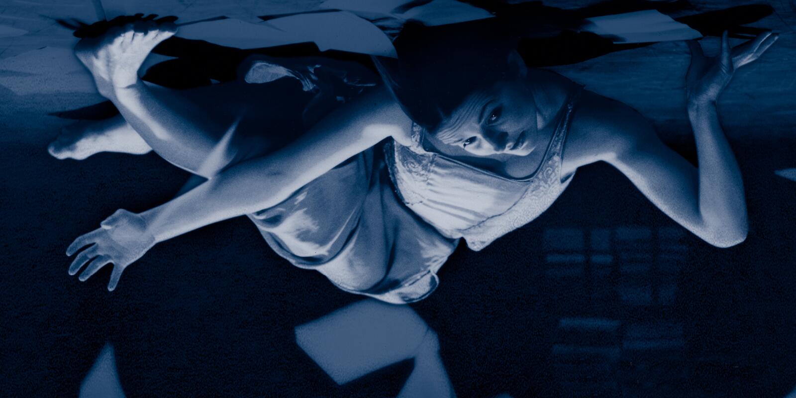 An upside-down image of a figure in movement on the floor among sheets of paper