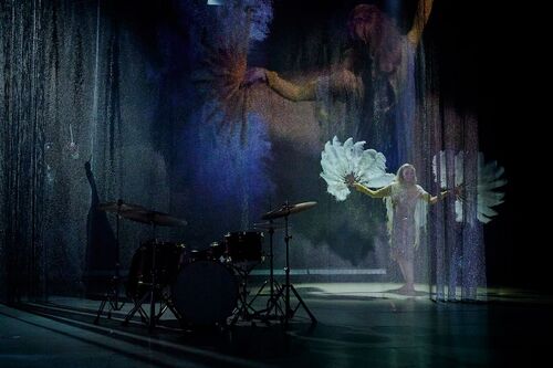 Justine Cooper spotlit on stage with feather fans in her hands