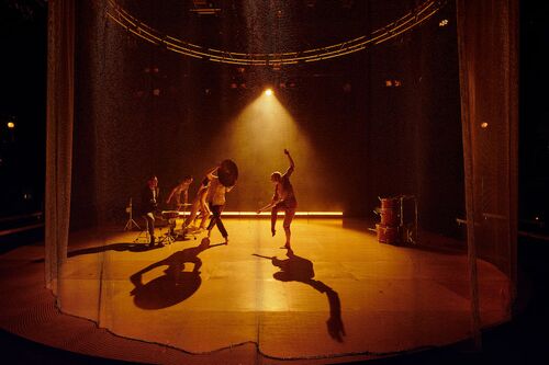 Two dancers in movement with a drum cymbal and a drummer at a drum-set