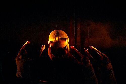 Four dancers in silhouette holding a cymbal aloft