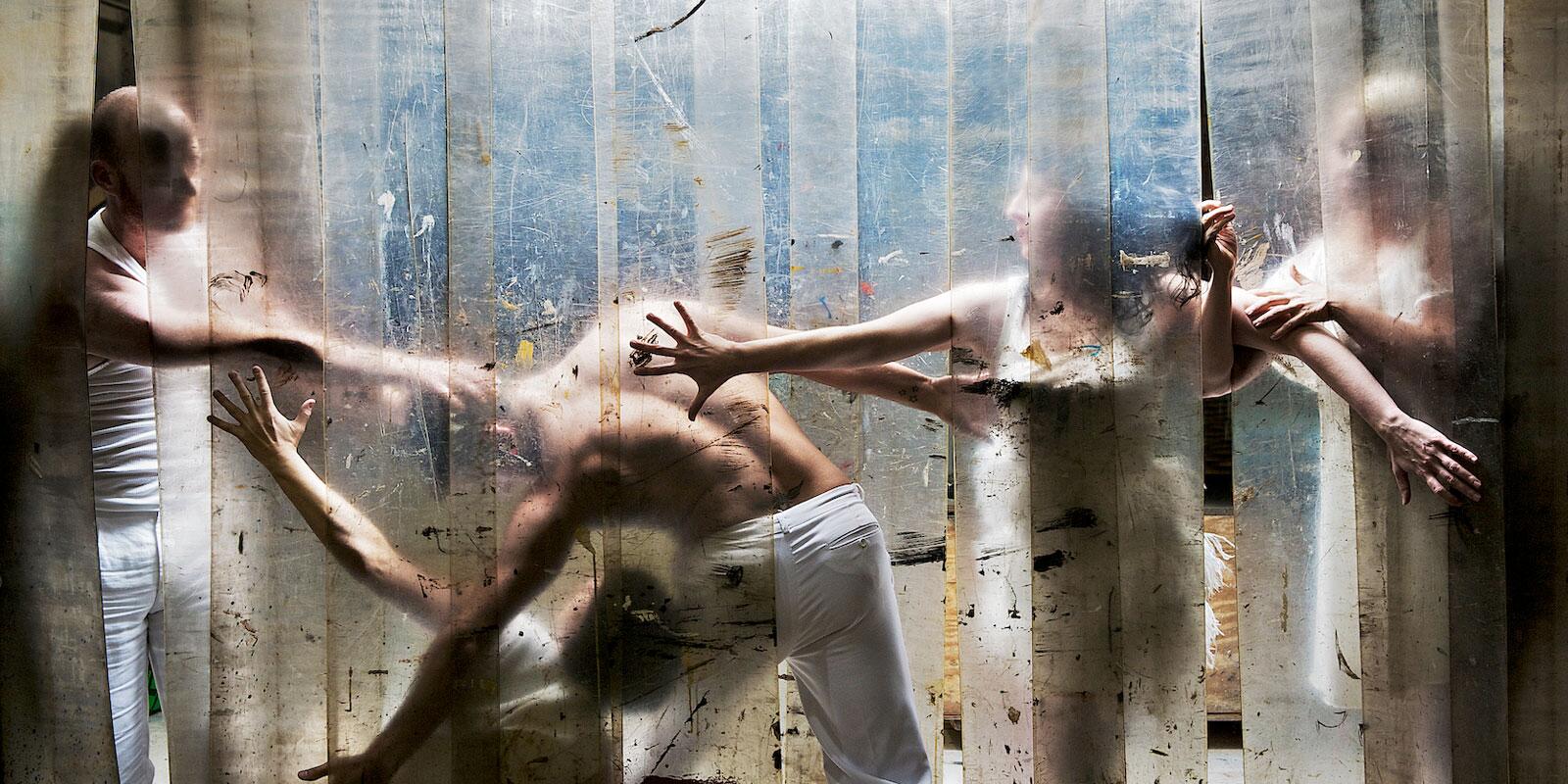 Five figures in movement behind a curtain of heavy plastic