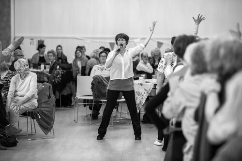 Philippa Donnellan in a room of participants speaking into a microphone with arms raised