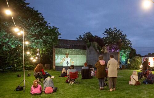 Audience gathered around a handball alley with projections cast on the back wall