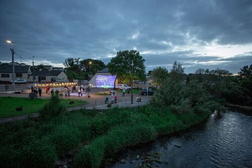 People gathered in a handball alley lit with projections seen from across the river