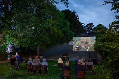 Audience seated around the opening of a handball alley with projections cast on the back wall