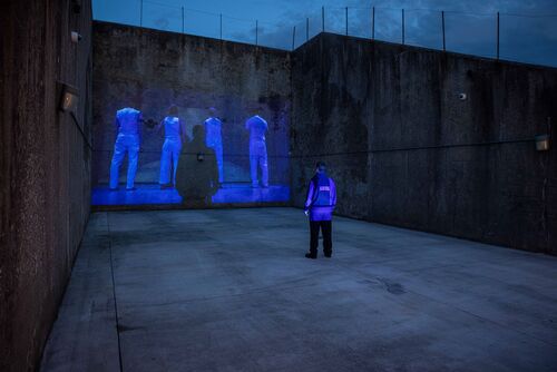 A figure standing in an empty handball alley with projects cast on the back wall