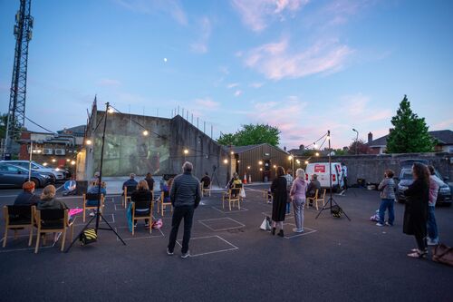 Audience standing and seated gathered around the opening of a handball alley