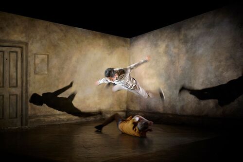 One dancer airborne jumping over another dancer rolling beneath