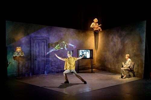 A dancer in movement centre stage, another sits side-stage and another is perched above the set