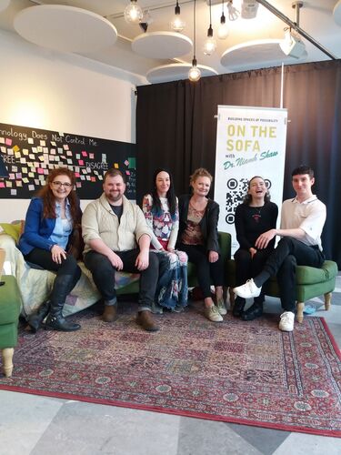 Six figures sitting on a large green couch smiling to camera