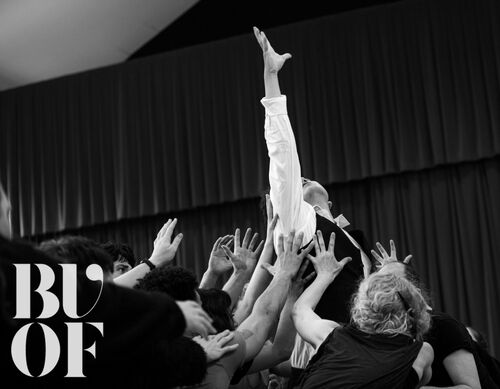 A single figure being lifted by the ensemble with their arm stretched upward