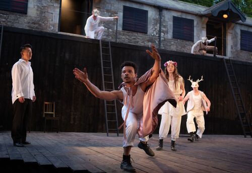 Four figures in movement with Vitor Bassi leaning and reaching both hands out towards the camera