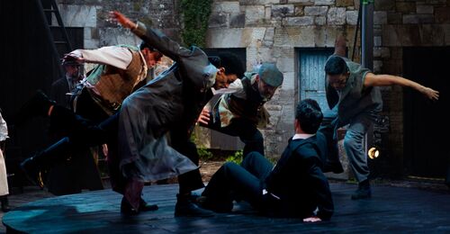 An ensemble of dancers in movement around a figure sitting on the floor