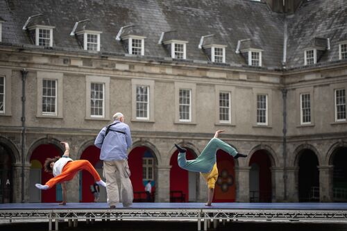 A still of two dancers breakdancing with a figure playing bodhrán between them