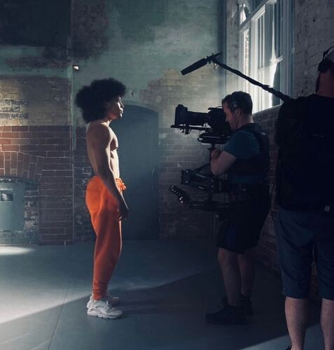 Cristian Emmanuel Dirocie standing in side profile facing a camera in the CoisCéim studio