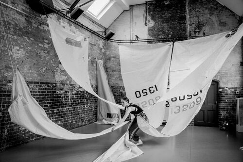 Rosie Stebbing in movement with large ship-sails attached to her waist, rigged to the ceiling