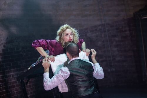 Justine Cooper lying along a table looking out as Jonathan Mitchell lifts the table