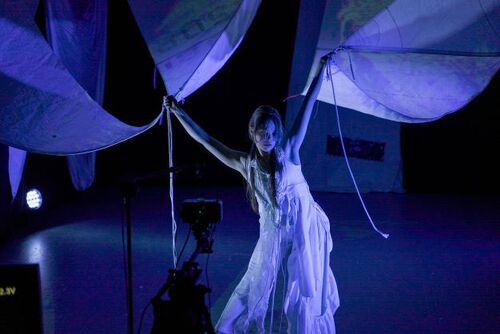Rosie Stebbing in movement holding the ends of sails above her head