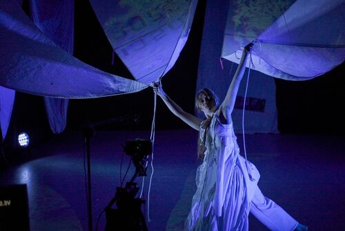 Rosie Stebbing in movement holding the ends of sails above her head