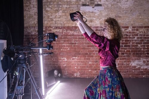 Justine Cooper in side profile facing the camera holding a VR headset aloft