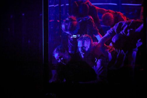 An ensemble of dancers lit in purple moving in one mass