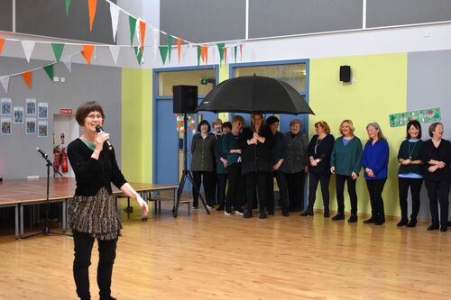 Philippa Donnellan speaking into a microphone with participants waiting in the background