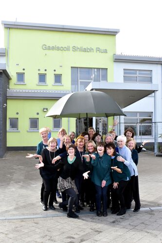 A group of participants outside Gaelscoil Shliabh Rua posing under an umbrella