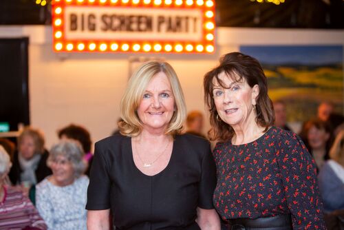 Participants smiling to camera with a sign for BIG SCREEN PARTY in the background
