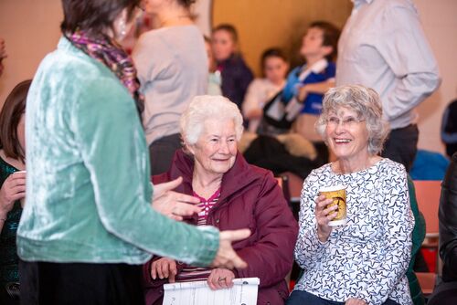 Participants seated holding a cup of tea and laughing