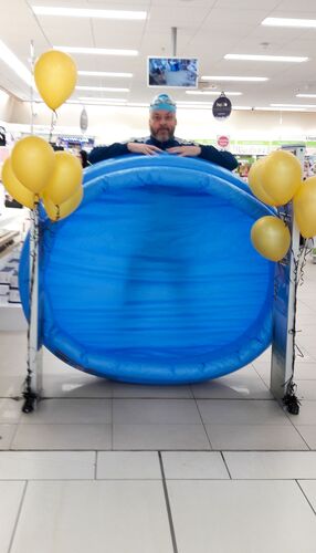 A man in a swim cap standing in the entrance to a supermarket with a blue inflatable pool