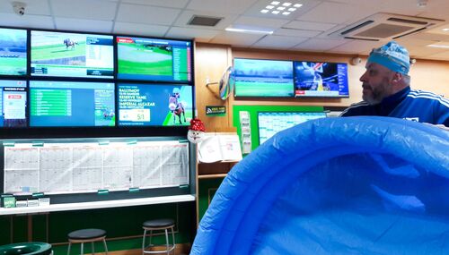 A man in a swim cap standing in a bookies with a blue inflatable pool