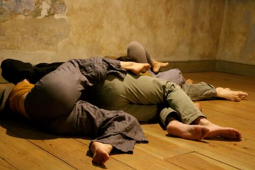 Three figures' legs entwined lying on the floor