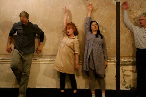 Four figures in movement against the wall of a room in a tenement house