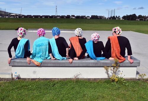 Participants in floral swim caps and orange and blue towels draped on their shoulders from behind