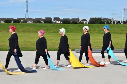 Participants costumed in black with floral swim caps trailing colourful towels behind them
