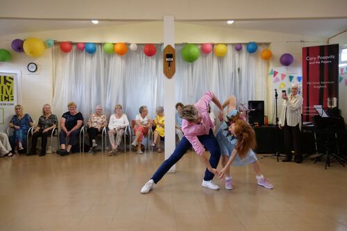 Two figures dancing a duet performing for audience seated in the background