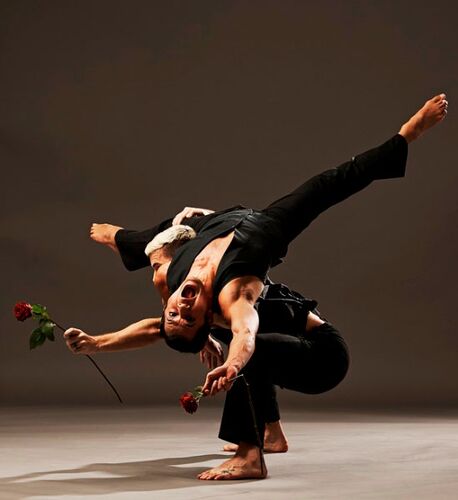 Two figures in movement with one rolling across the others back