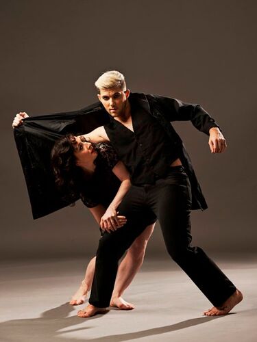 Two figures in movement together with one tucked under the others jacket