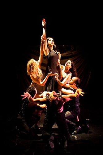 An ensemble in movement gathered together with one figure reaching upwards at the centre