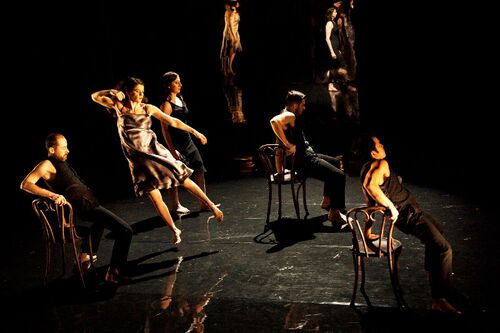 Five figures in movement on stage, three on chairs, one mid-jump and the last upright
