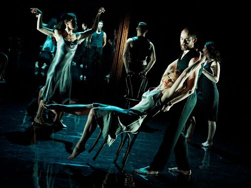 An ensemble in movement with one figure leaning backwards in a wooden chair