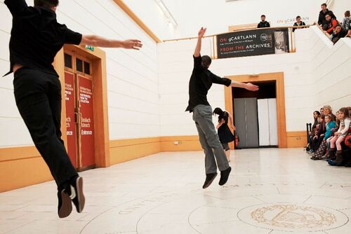 Two figures airborne mid-jump and another in movement in a bright gallery space