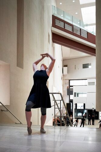 A figure in movement with arms raised upward in an open gallery space