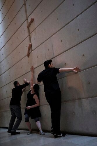 Three figures in movement against a large concrete wall