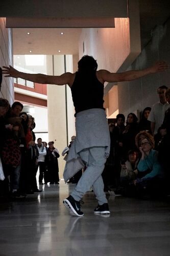 A figure in movement in front of an audience in a gallery space