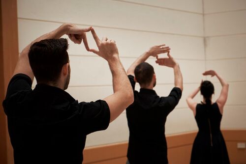 Three figures with arms raised above their heads in hand gestures in a gallery space
