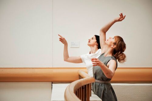 Two figures in side profile at the edge of a balcony in movement