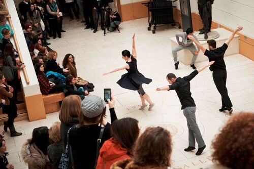 Three dancers in movement in front of an audience in a gallery space