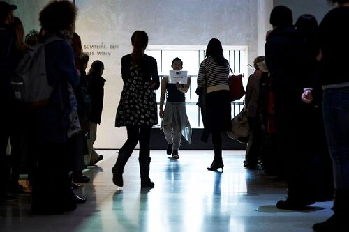 A figure backlit performing with audience standing surrounding